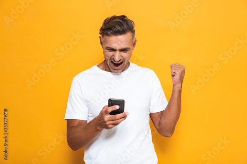 Happy man posing isolated over yellow wall background using mobile phone. © Drobot Dean