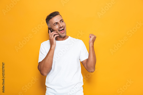Emotional man posing isolated over yellow wall background talking by mobile phone. © Drobot Dean