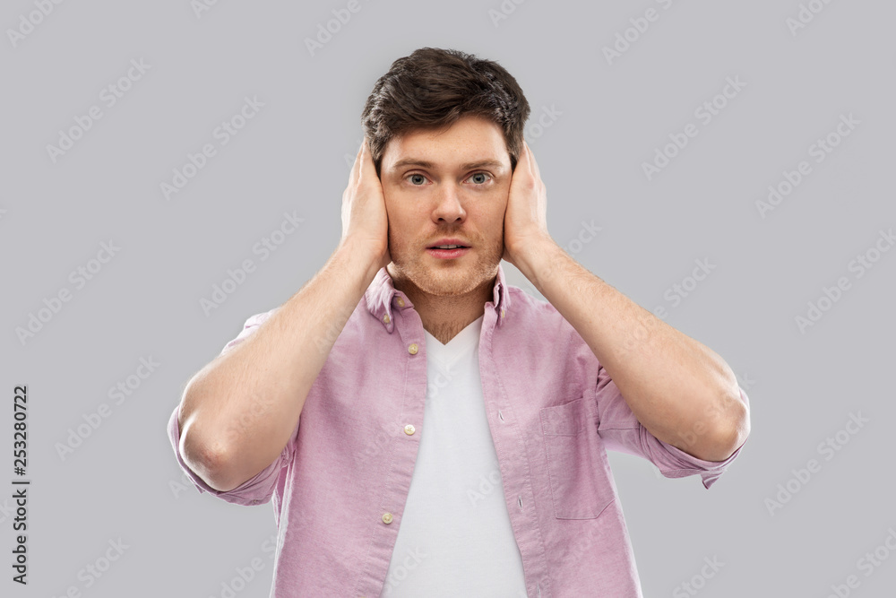 Naklejka premium people, noise and stress concept - man closing ears by hands over grey background