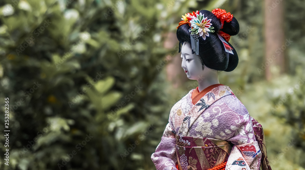 Close-up of a traditional Japanese porcelain doll with a colorful silk kimono with embroideries Close-up of a traditional Japanese porcelain doll with a colorful silk kimono with embroideries