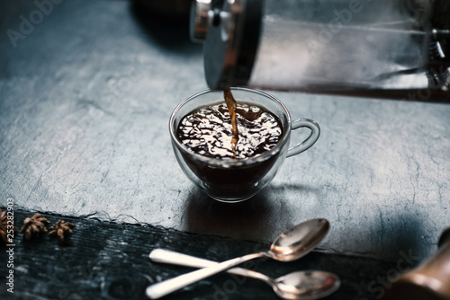 Pouring a coffee from french press to coffee mug on a stone, dark background. 