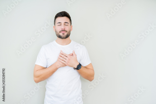 Young handsome man wearing casual white t-shirt over isolated background smiling with hands on chest with closed eyes and grateful gesture on face. Health concept. © Krakenimages.com