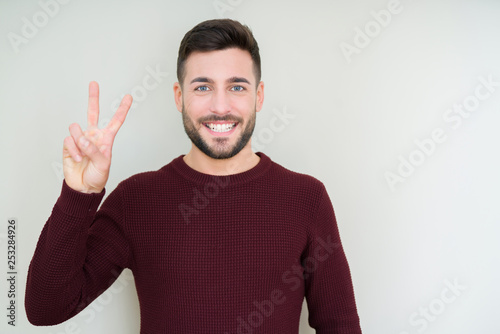 Young handsome man wearing a sweater over isolated background showing and pointing up with fingers number two while smiling confident and happy.