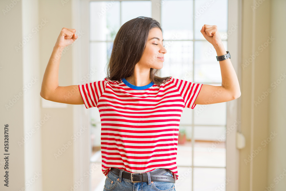 Young beautiful woman wearing casual t-shirt showing arms muscles smiling proud. Fitness concept. Young beautiful woman wearing casual t-shirt showing arms muscles smiling proud. Fitness concept.