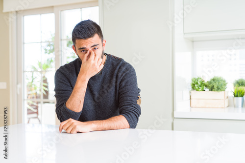 Handsome hispanic man wearing casual sweater at home tired rubbing nose and eyes feeling fatigue and headache. Stress and frustration concept.