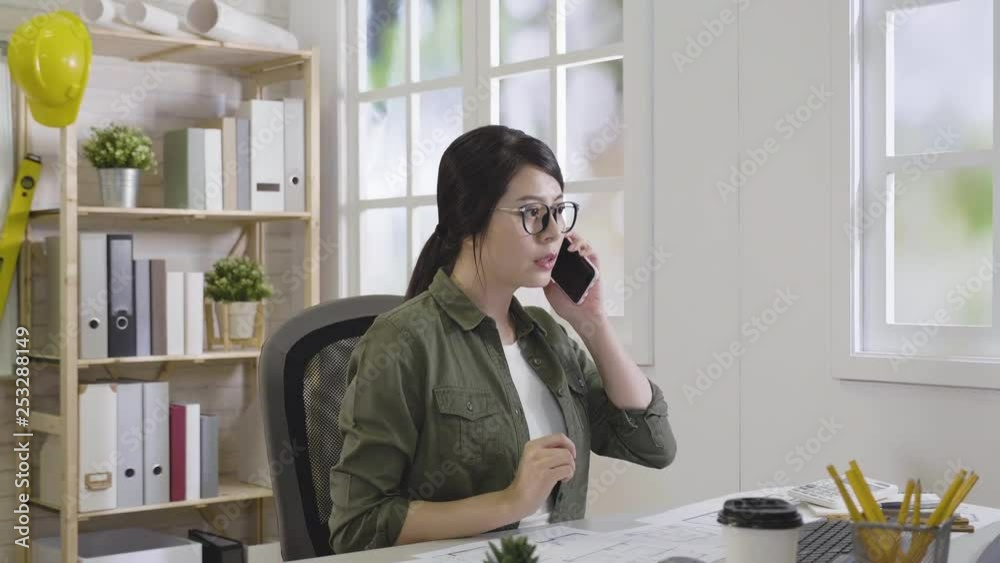 confident female construction worker pick up cellphone prepared walk out from office fast. young lady architect put on safety vest and hard hat going to work helping partner. modern work place.