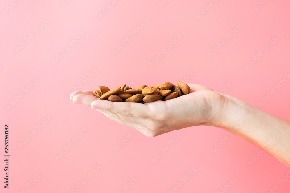 Young woman hand holding almonds on isolated pink background. Young woman hand holding almonds on isolated pink background.