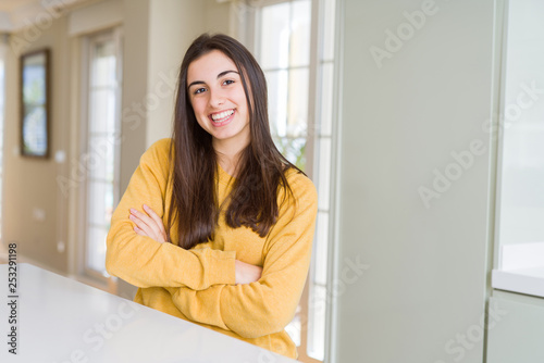 Beautiful young woman wearing yellow sweater happy face smiling with crossed arms looking at the camera. Positive person.