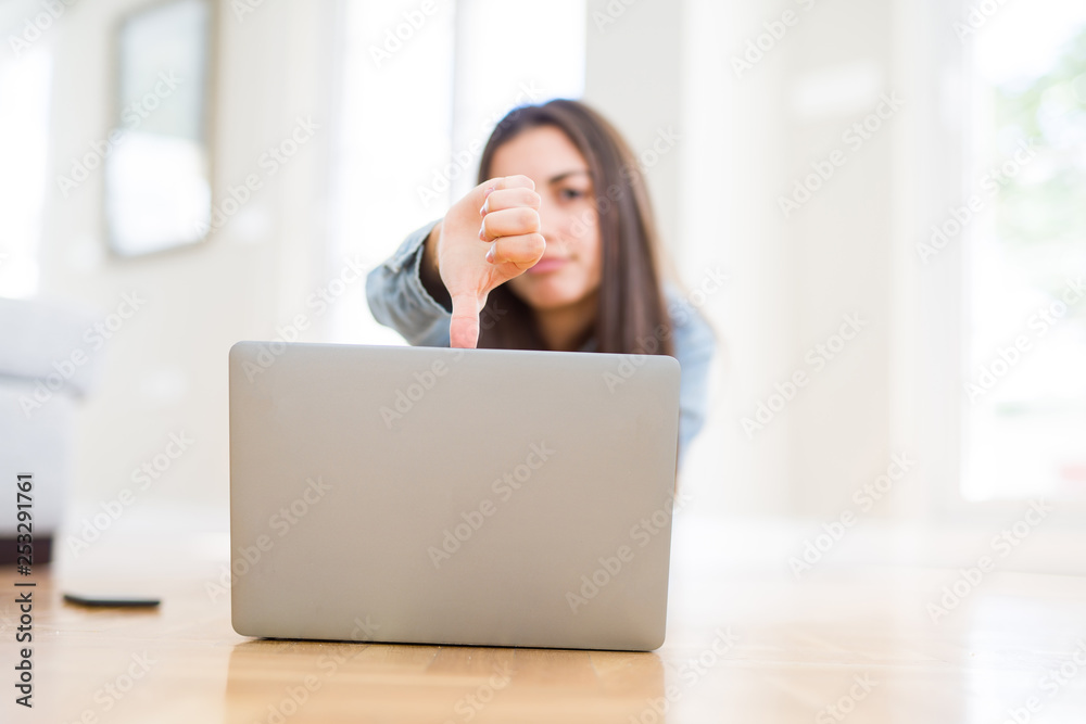 Beautiful young woman laying on the floor using laptop with angry face, negative sign showing dislike with thumbs down, rejection concept Beautiful young woman laying on the floor using laptop with angry face, negative sign showing dislike with thumbs down, rejection concept