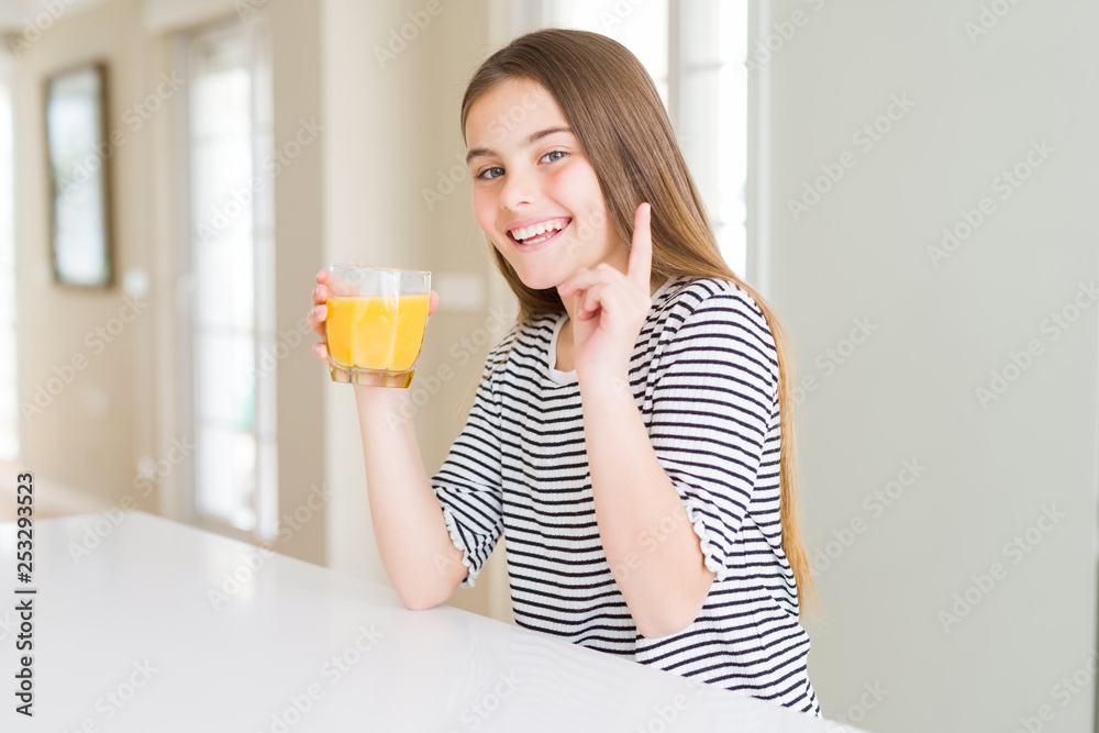 Beautiful young girl kid drinking a glass of fresh orange juice surprised with an idea or question pointing finger with happy face, number one Beautiful young girl kid drinking a glass of fresh orange juice surprised with an idea or question pointing finger with happy face, number one