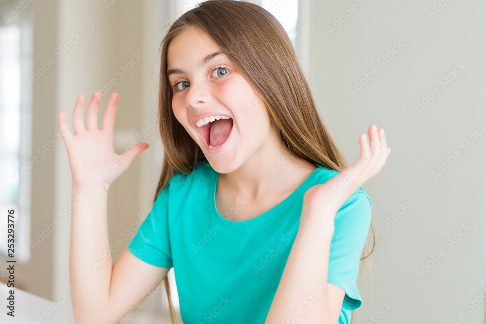 Beautiful young girl kid wearing green t-shirt celebrating crazy and amazed for success with arms raised and open eyes screaming excited. Winner concept Beautiful young girl kid wearing green t-shirt celebrating crazy and amazed for success with arms raised and open eyes screaming excited. Winner concept