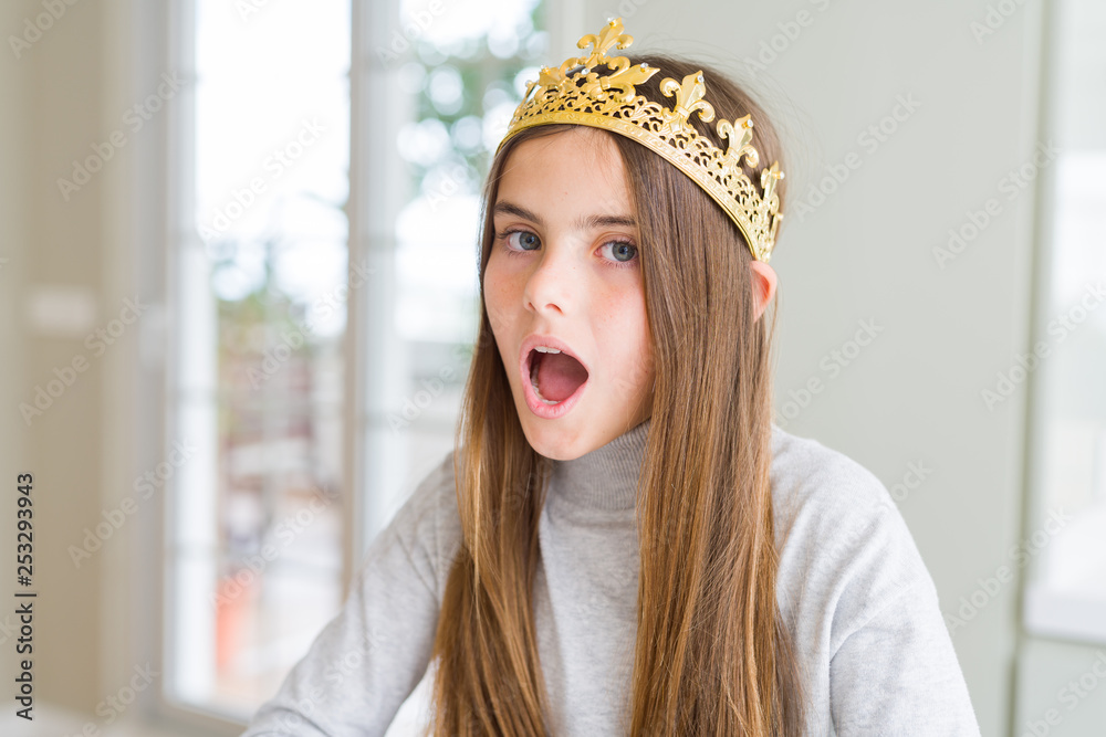 Beautiful young girl wearing a golden crown as a princess from fairytale afraid and shocked with surprise expression, fear and excited face. Beautiful young girl wearing a golden crown as a princess from fairytale afraid and shocked with surprise expression, fear and excited face.