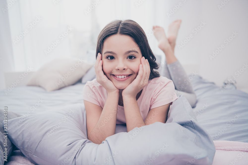 Close up photo beautiful she her little girl curly wavy lying down pillow hands arms hold head homey sunday mood wear home t-shirt pants comfortable apartments flat bright light colored room