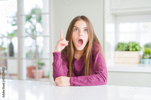 Beautiful young girl kid on white table pointing finger up with successful idea. Exited and happy. Number one.