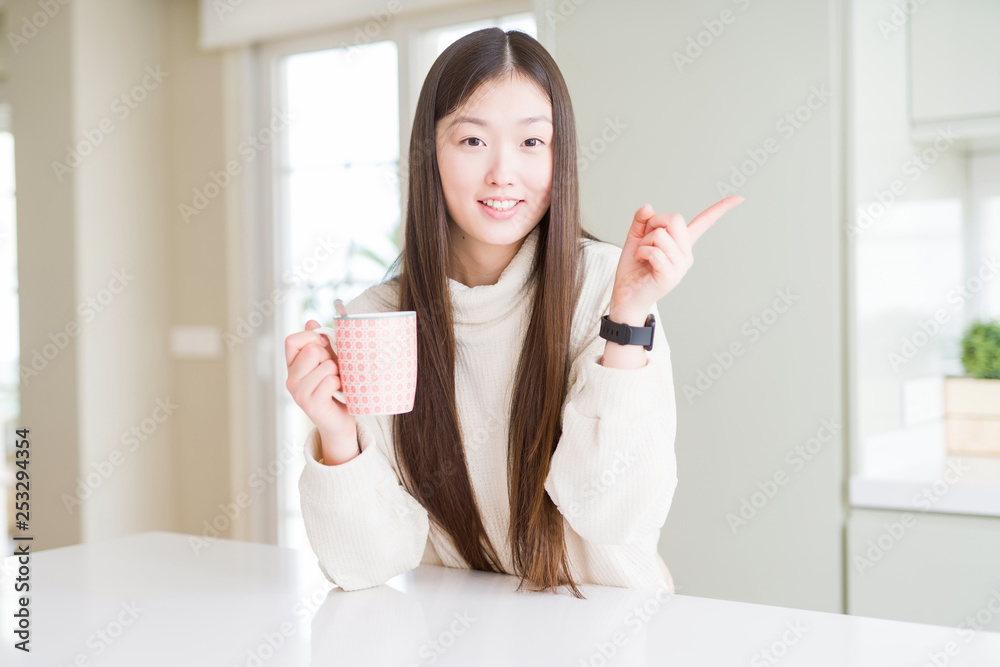 Beautiful Asian woman drinking a cup of coffee very happy pointing with hand and finger to the side Beautiful Asian woman drinking a cup of coffee very happy pointing with hand and finger to the side