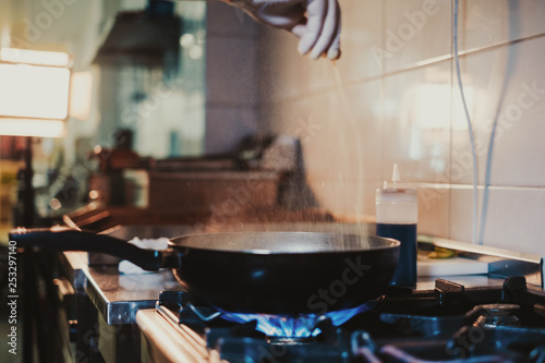 Kitchen chef adding salt in frying pan