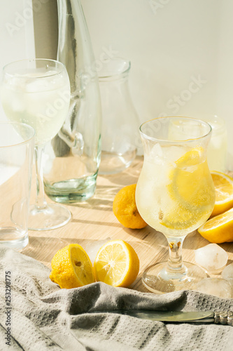 Summer refreshing drink of fresh lemon and ice cubes in transparent glass a light background. Homemade mahito or detox.