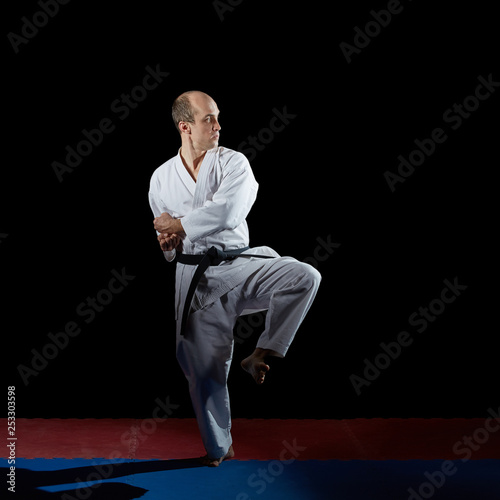On a red and blue tatami adult athlete performs formal karate exercises