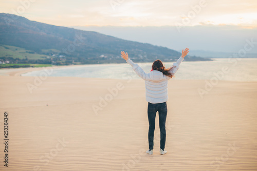 Young girl enjoying ocean view with open hands on sunrise (Tarifa, Spain) - concept of travelling and freedom