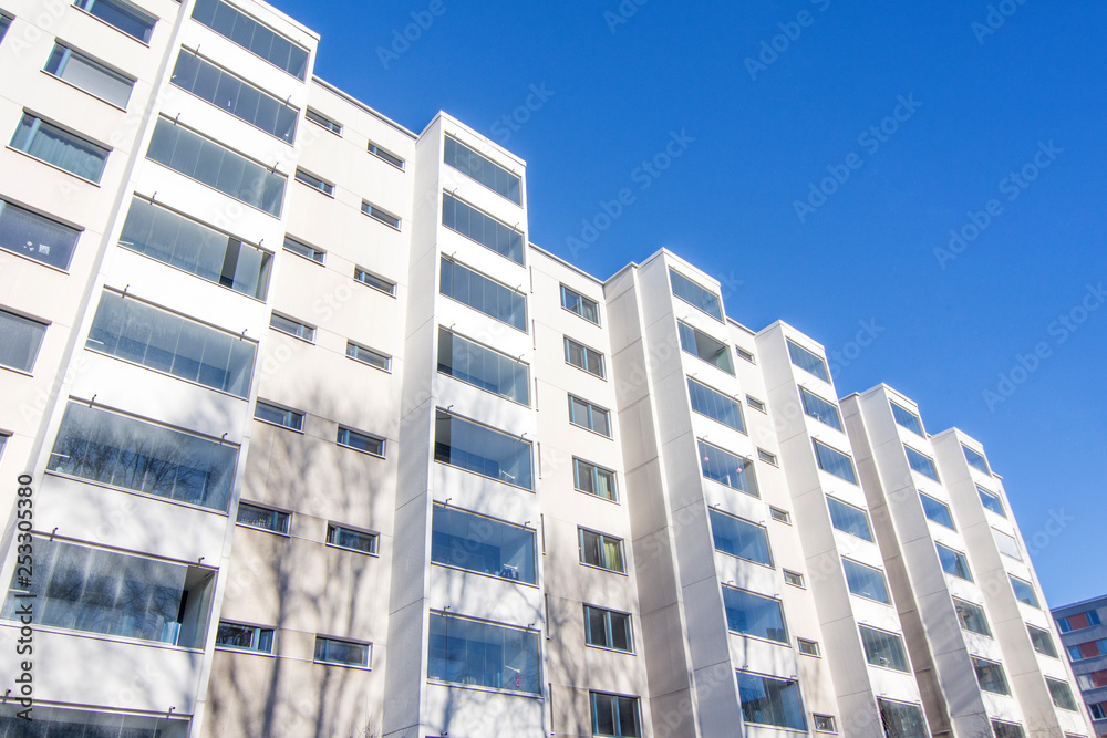 White multi-storey residential building with glazed frameless windows and balconies White multi-storey residential building with glazed frameless windows and balconies
