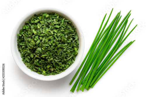 Dried chopped chives in white ceramic bowl next to a pile of whole fresh chives isolated on white from above. photo