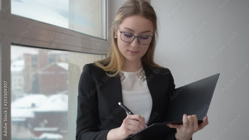 Young woman entrepreneur thinking and writing business document near window. Business woman looking to window and doing notes in document paper. Business people concept
