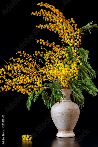 On the table is a vase with mimosa on a black background.