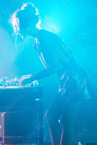 beautiful dj woman with blonde hair using dj mixer in nightclub with smoke