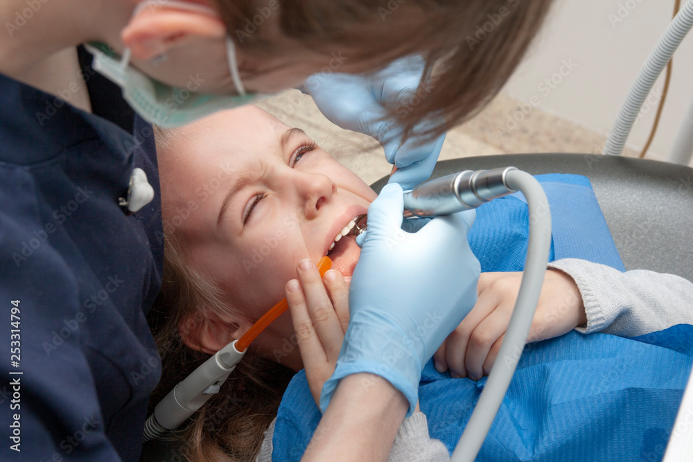 A dentist with a rubber glove is repairing a tooth for a little girl A dentist with a rubber glove is repairing a tooth for a little girl