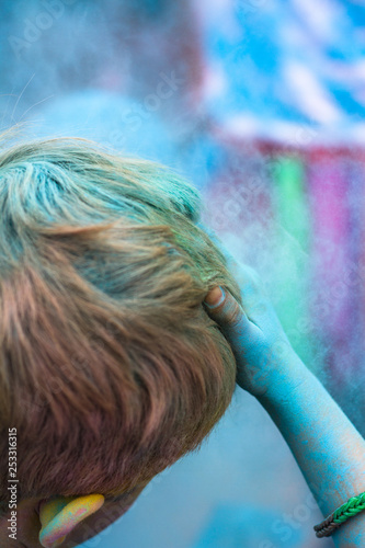 Fototapeta Naklejka Na Ścianę i Meble -  Red haired person holds blue paint covered hand to their head after completing a Colour Paint Run in aid of charity.