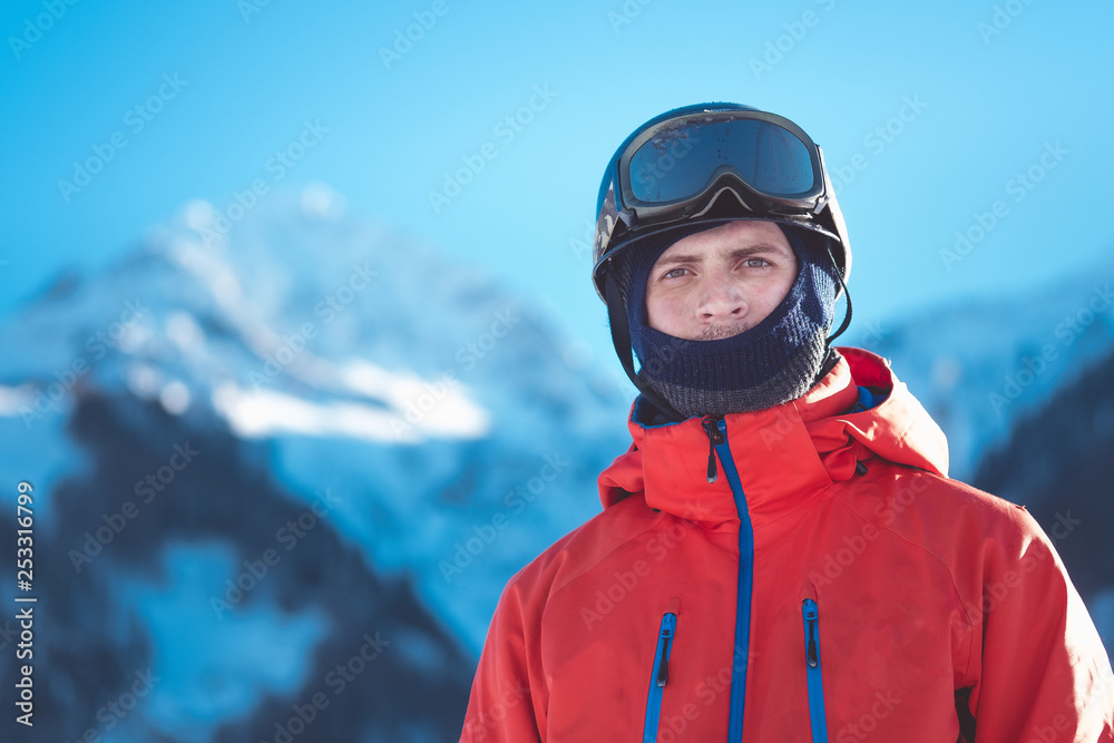 Portrait: A professional rider in a ski helmet stands against the backdrop of mountains and snowy peaks