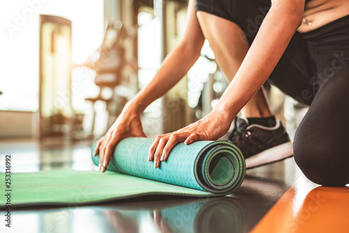 Obraz na plátně Close up of sporty woman folding yoga mattress in sport fitness gym training center background