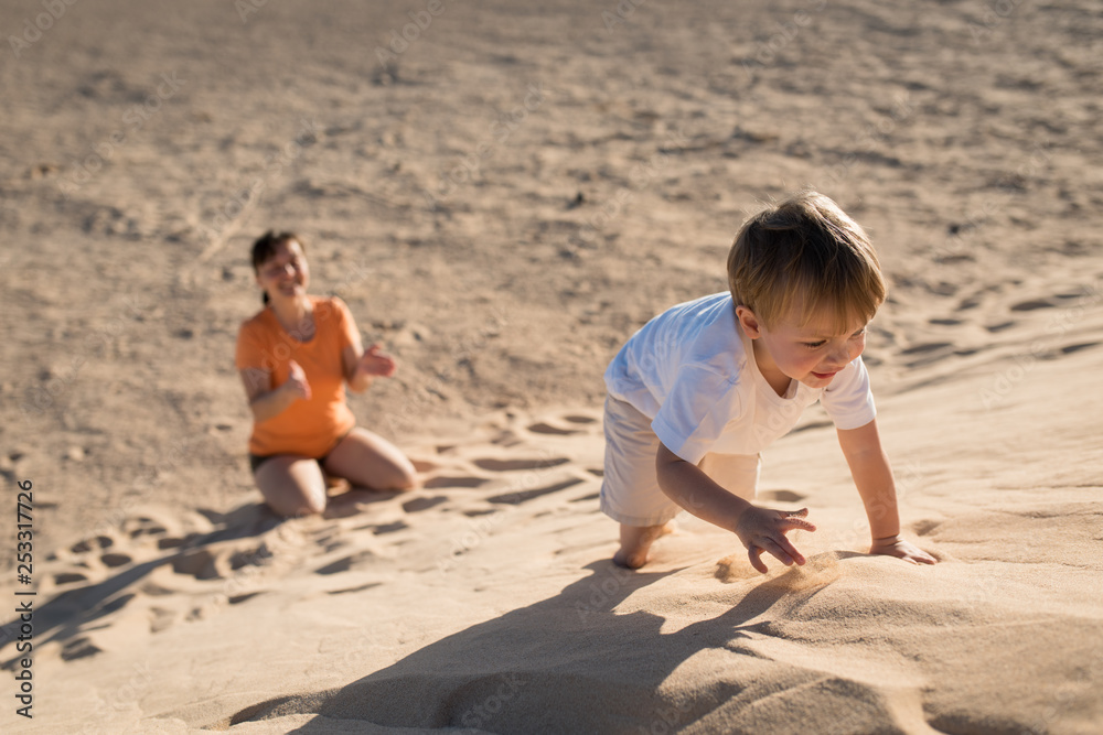 Handsome baby boy climbing on a sand dune with mother. Handsome baby boy climbing on a sand dune with mother.