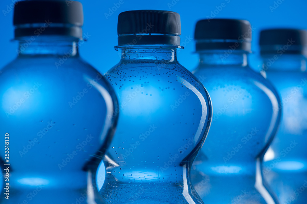 close up of transparent plastic water bottles with bubbles in row on blue background close up of transparent plastic water bottles with bubbles in row on blue background