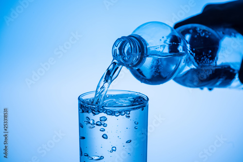 partial view of man pouring water from plastic bottle in glass on blue background