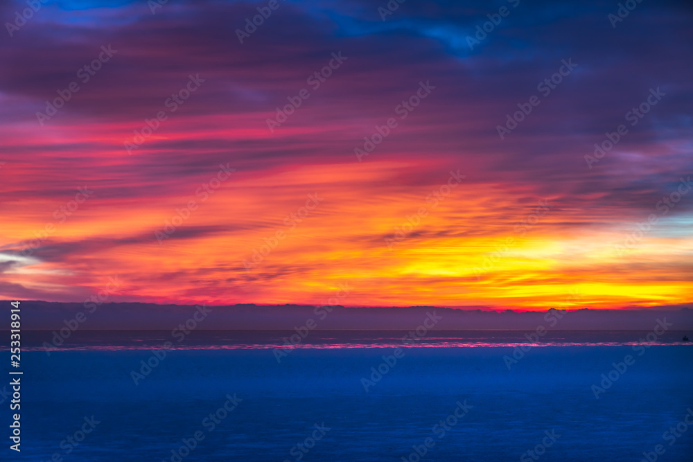 Gorgeous dramatic closeup sunrise photograph of the blue waters of Lake Michigan with orange, yellow, pink, purple and blue clouds in the sky above making a beautiful background. Gorgeous dramatic closeup sunrise photograph of the blue waters of Lake Michigan with orange, yellow, pink, purple and blue clouds in the sky above making a beautiful background.