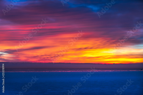 Gorgeous dramatic closeup sunrise photograph of the blue waters of Lake Michigan with orange, yellow, pink, purple and blue clouds in the sky above making a beautiful background.