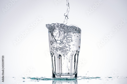 water pouring in glass on white background with backlit, splashes and copy space