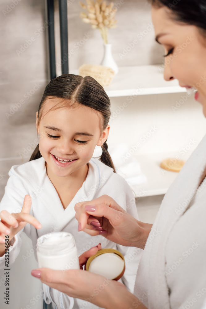 selective focus of daughter touching cosmetic cream in mother hand in bathroom selective focus of daughter touching cosmetic cream in mother hand in bathroom