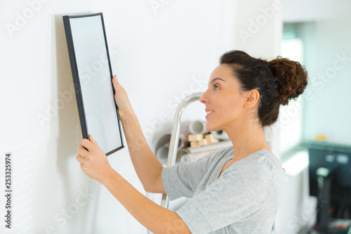 young woman hanging a picture on the wall