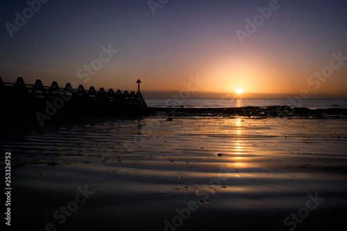 Sun rising over the sea with sand and sea defences. photo