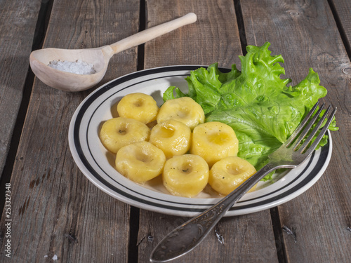 Hot lunch of potato gnocchi with leaves of fresh leaf lettuce on a ceramic plate with stripes, shot from close range on a plank rustic table.