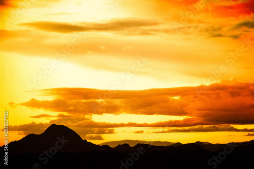 Clouds reflecting the light of a colorful sunset with a distant mountain at the bottom of the image.