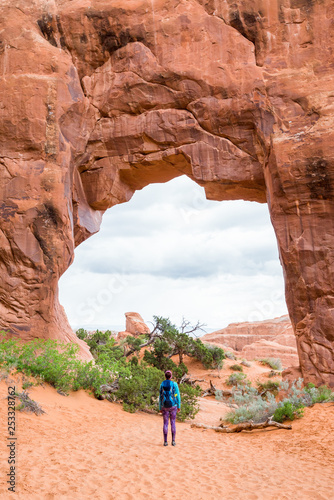 Young woman is looking at the Pine Tree Arch at Devils Garden Arches National Park Moab Utah. Travel and adventure concept. Hiking concept.