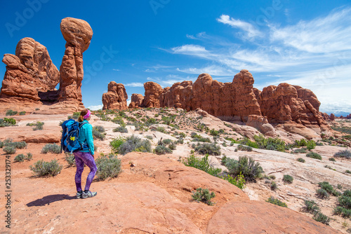 Young woman wearing backpack is looking at the Garden of Eden in Arches National Park in Utah. Female hiker in Arches National Park. Travel and adventure concept.