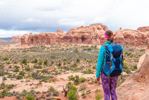 Young woman wearing backpack is looking at the Parade of Elephants in Arches National Park in Utah. Female hiker in Arches National Park. Travel and adventure concept.