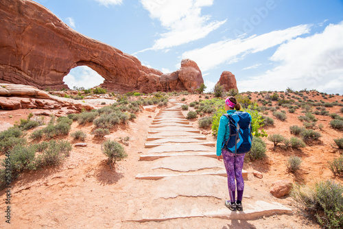 Young woman wearing backpack is looking at the North Window at Arches National Park in Utah. Female hiker in Arches National Park. Travel and adventure concept. © blazekg