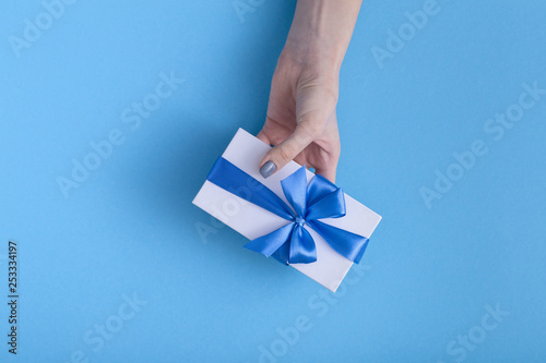 girl holding a beautiful present in hands, women with gift box with a tied blue ribbon bow in hands on a pastel colored background, top view, concept holiday, love and care