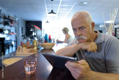 senior man sat at the bar looking at a tablet