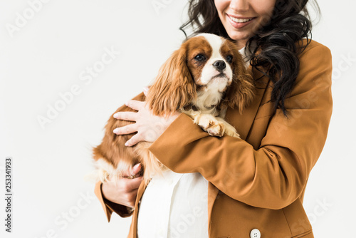 Cropped view of laughing pregnant woman in brown jacket holding dog isolated on white